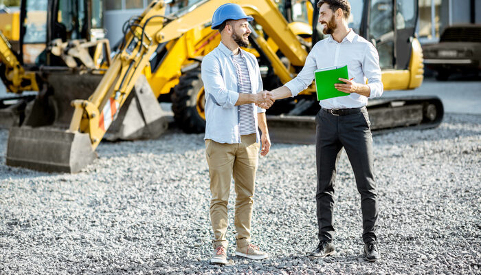 Builder choosing heavy machinery for construction with a sales consultant shaking hands on the open ground of a shop with special vehicles