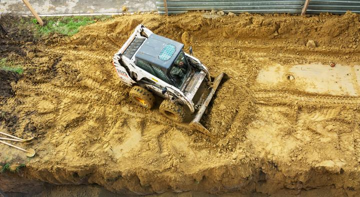 A small tractor works in the sand, filling up a hole