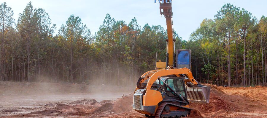 Heavy machinery grades land at a construction site surrounded by trees