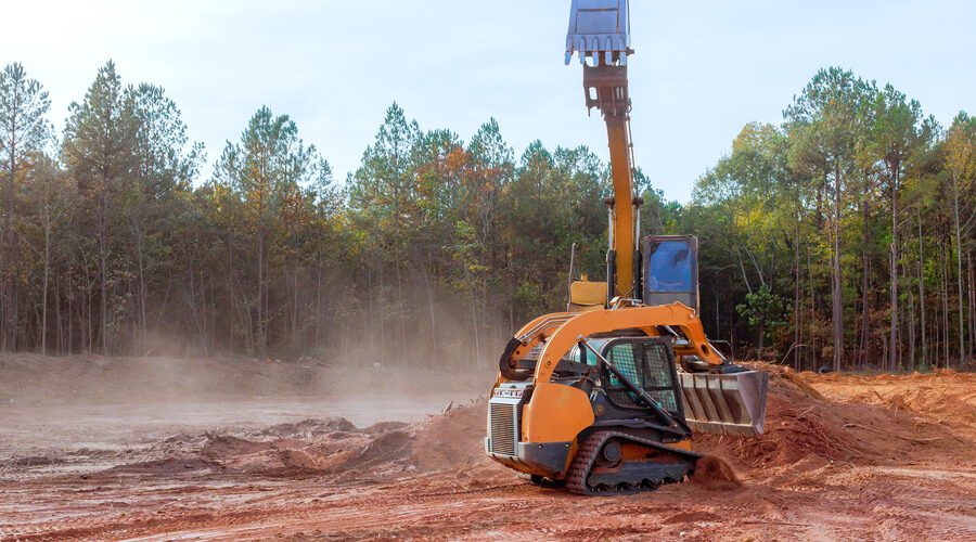 Heavy machinery grades land at a construction site surrounded by trees