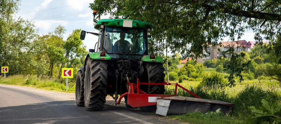 Big modern industrial tractor machine cutting green grass with mowing equipment along country roadside