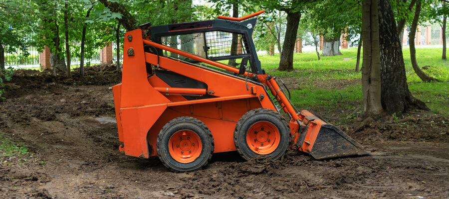 Mini bulldozer or skid steer loader working with earth in public park and performing landscaping works