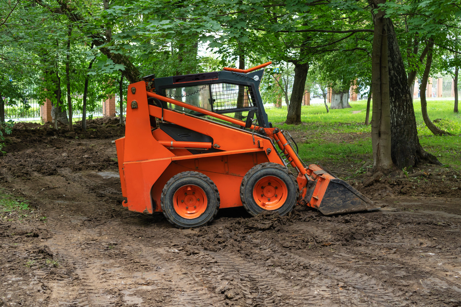 Mini bulldozer or skid steer loader working with earth in public park and performing landscaping works