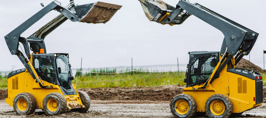 two yellow skid steers with raiced bucket outdoors