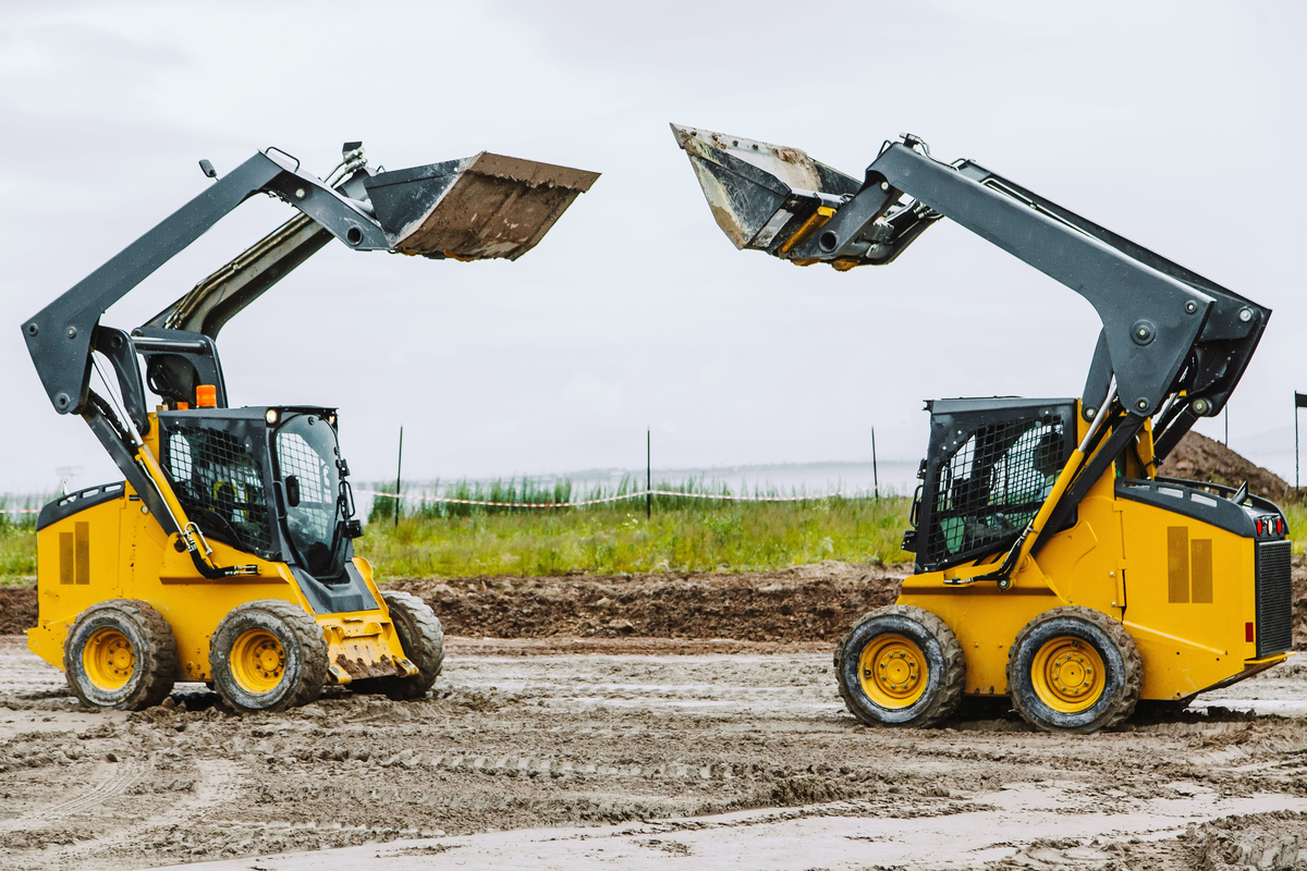 two yellow skid steers with raiced bucket outdoors